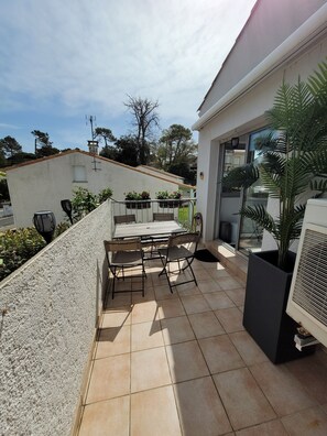 Une terrasse avec une table et des chaises, un pot de fleurs et un grand appareil de climatisation.