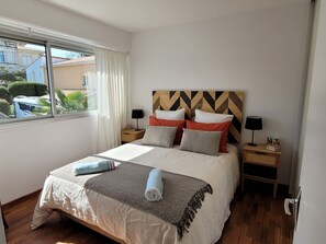 Un lit bien fait, recouvert d’un couvre-lit à motifs, deux tables de chevet avec des lampes et une fenêtre avec des rideaux.