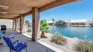 Un patio techado con piscina, sillas reclinables azules y vista a un edificio al otro lado del agua.