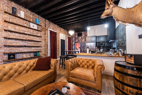 A modern living room with a brick wall, leather sofas, a wooden coffee table, and a mounted deer head.