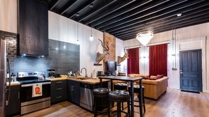 A modern kitchen with a central island, stainless steel appliances, and a brick accent wall. - The Rickhouse in NuLu~2 King Bed/2 Full Bath (Louisville)