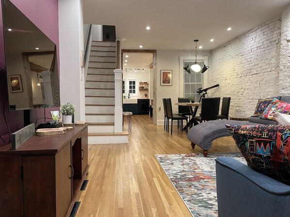 Una sala de estar moderna con escalera, piso de madera y un comedor.