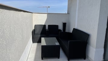 Un patio en la azotea con mobiliario de ratán negro, incluyendo un sofá, sillones y una mesita.