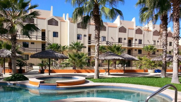 A resort pool area with a hot tub, palm trees, and a building with arched windows.