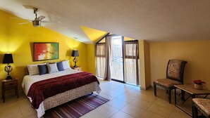 A bedroom with a bed, a chair, a table, a ceiling fan, and a window with curtains.