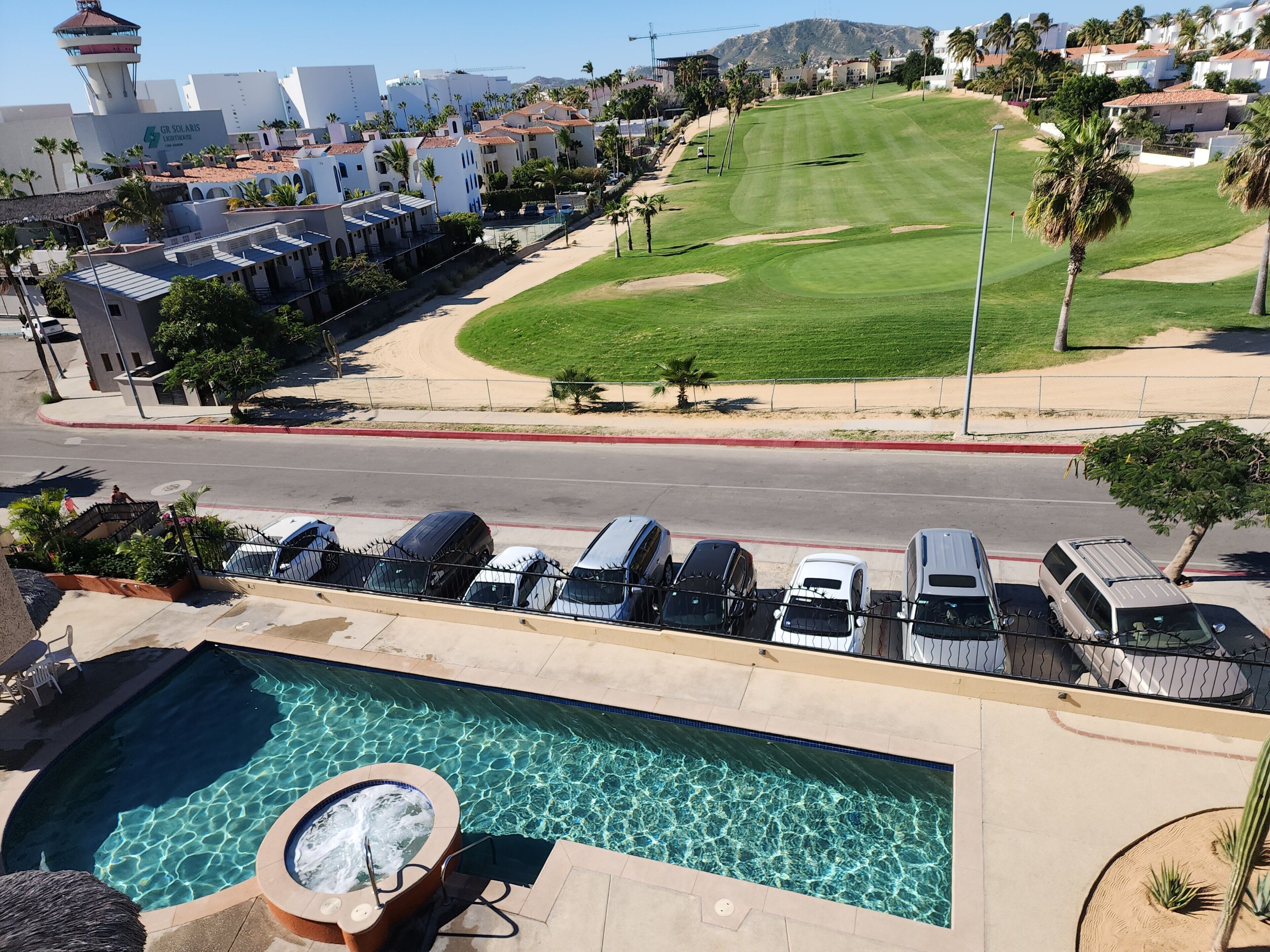 Une piscine avec un jacuzzi, un terrain de golf et un parking avec des voitures.