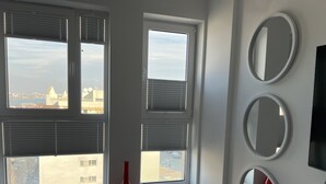 Ein Zimmer mit großen Fenstern, einer roten Vase und drei Wandspiegeln.