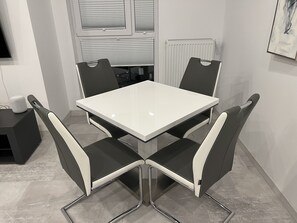 Ein zeitgemäßer Essbereich mit einem weißen Tisch und schwarz-weißen Stühlen, einem Heizkörper und einem Fenster mit Jalousien.