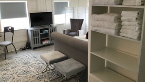 Una sala de estar con televisor, sofá, otomanes y un estante con toallas.