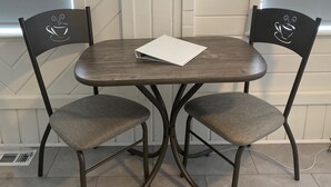 Una pequeña mesa de comedor con dos sillas, una libreta blanca y un panel decorativo en la pared.