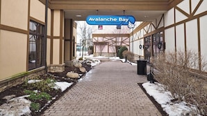 Entrada a un parque acuático interior con un camino de ladrillo, parches de nieve y un letrero de Avalanche Bay.