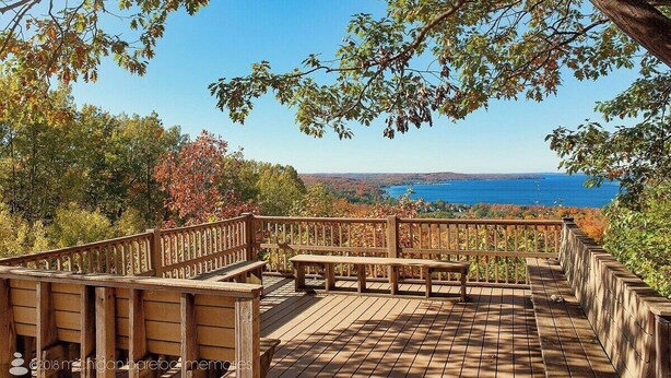Terraza de madera con bancos que ofrece una vista panorámica de un lago y un bosque.