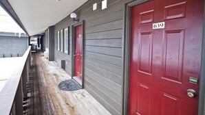 Un porche cubierto con una puerta roja marcada con el número 639, una terraza de madera y una fachada de edificio gris.
