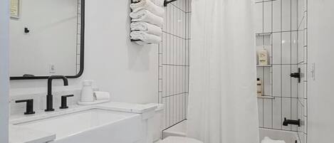 A modern bathroom with a white sink, black faucets, a toilet, and a shower with a white curtain.