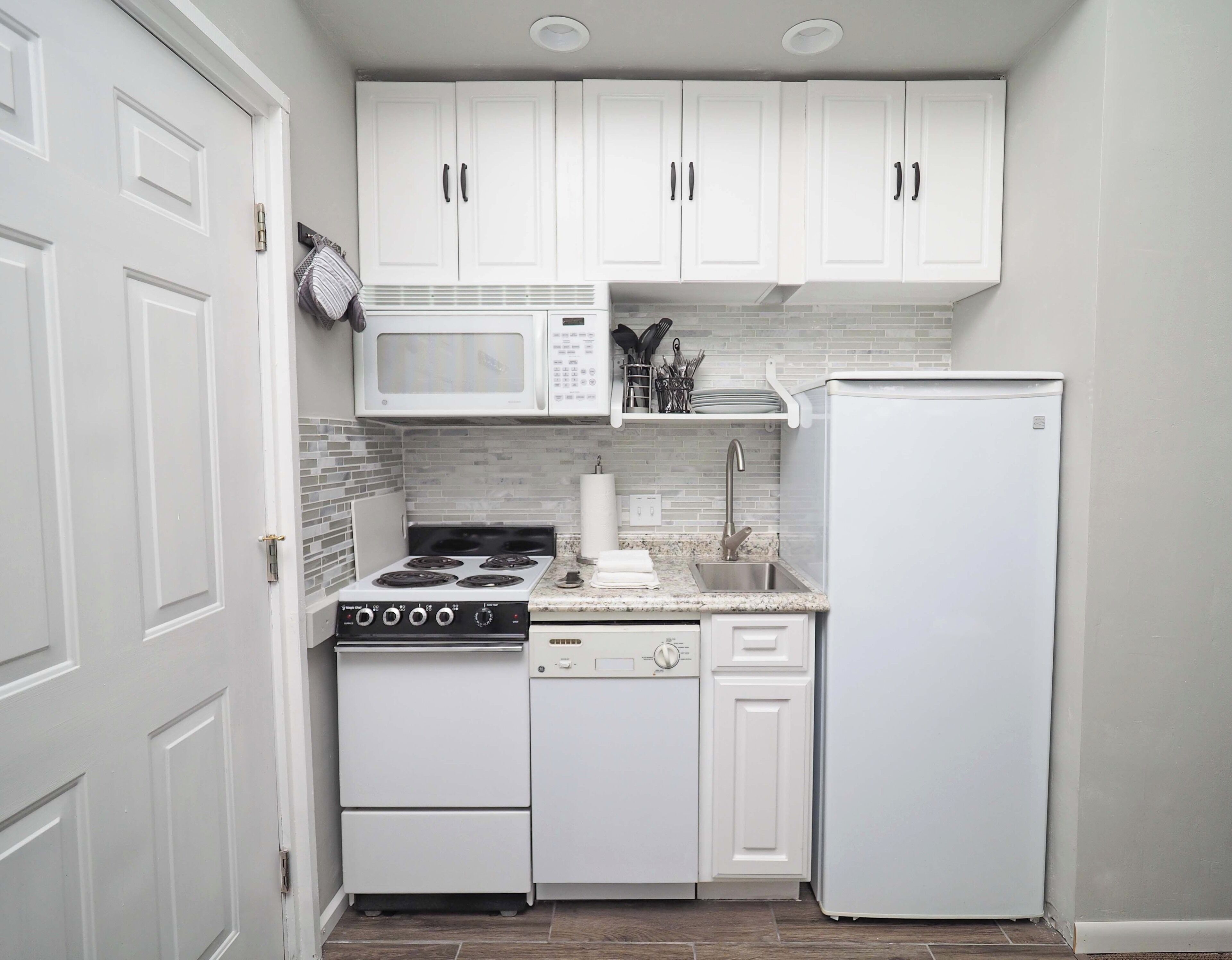 A compact kitchen with white cabinetry, a microwave, stove, dishwasher, and a refrigerator.