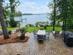 Patio esterno con tavolo e sedie, un barbecue e vista su un lago con pontili.