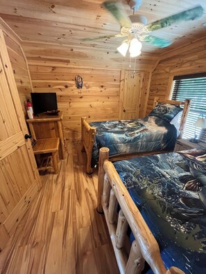 A wooden cabin room with two beds, a ceiling fan, a TV, and a small table. - DREHER DREAMS CABIN-LAKEFRONT- + FISHING, KAYAKS,PADDLEBOARDS, 7 BEDS SLEEPS 9!  (Prosperity)