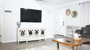 Een woonkamer met een flatscreen-tv aan de muur, een witte kast met ronde uitsparingen, een houten salontafel en een grijze bank.