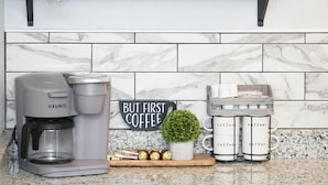 Een keuken met een koffiezetapparaat, mokken en decoratieve accessoires op het aanrecht.