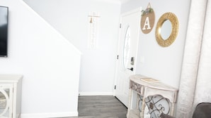 Een hal met een trap, een witte deur en een console tafel met een boek en een zakdoos.