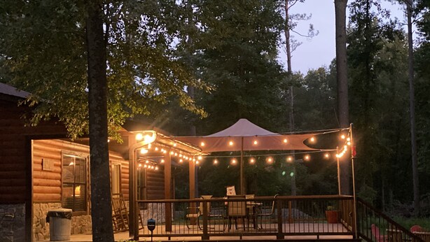 Eine Holzhütte mit einer überdachten Terrasse, Lichterketten und einer Treppe zum Eingang.