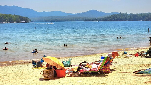 Ein Strand mit klarem, blauem Wasser, Menschen beim Schwimmen und Liegestühlen mit Sonnenschirmen.