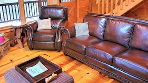 Ein gemütliches Blockhaus-Interieur mit Holzboden, Ledersofas, einer Holztreppe und großen Fenstern.