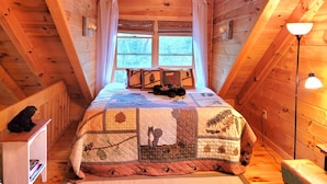 Ein gemütliches Schlafzimmer unter dem Dach mit Holzbalken, einem großen Fenster und einer gesteppten Bettdecke.