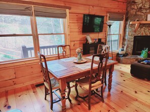A wooden cabin with a dining table, chairs, a television, and a fireplace. - LUXURY WATWRVIEW CABIN WITH 2 FIREPLACES (Blue Ridge)
