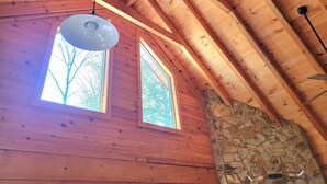 Ein Holzblockbau-Innenraum mit Kamin aus Stein, zwei Fenstern und einer geneigten Decke.
