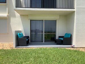 A balcony with two black sofas and blue cushions, a sliding glass door, and a view of a grassy area.