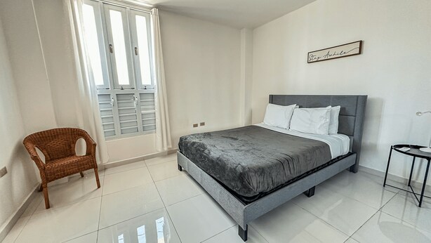 Une chambre à coucher avec un lit, une chaise, une table de chevet et une fenêtre avec des rideaux.