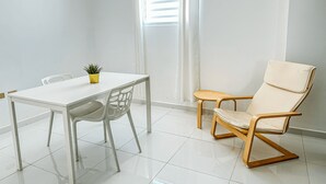 Une pièce au décor minimaliste, avec une table blanche, une plante en pot, une chaise en bois et une fenêtre avec des stores.