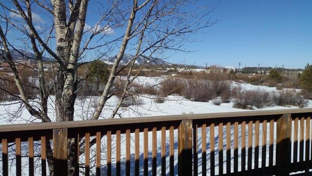 Une terrasse en bois offrant une vue sur un paysage enneigé, avec des arbres et des montagnes au loin.