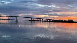 A bridge over calm water with a sunset sky.