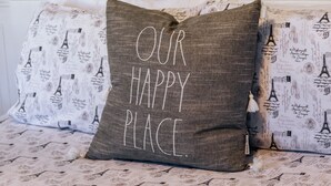 A bed with pillows featuring the Eiffel Tower and the text "OUR HAPPY PLACE."