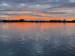 A calm body of water reflecting a sunset sky with a bridge and distant buildings.