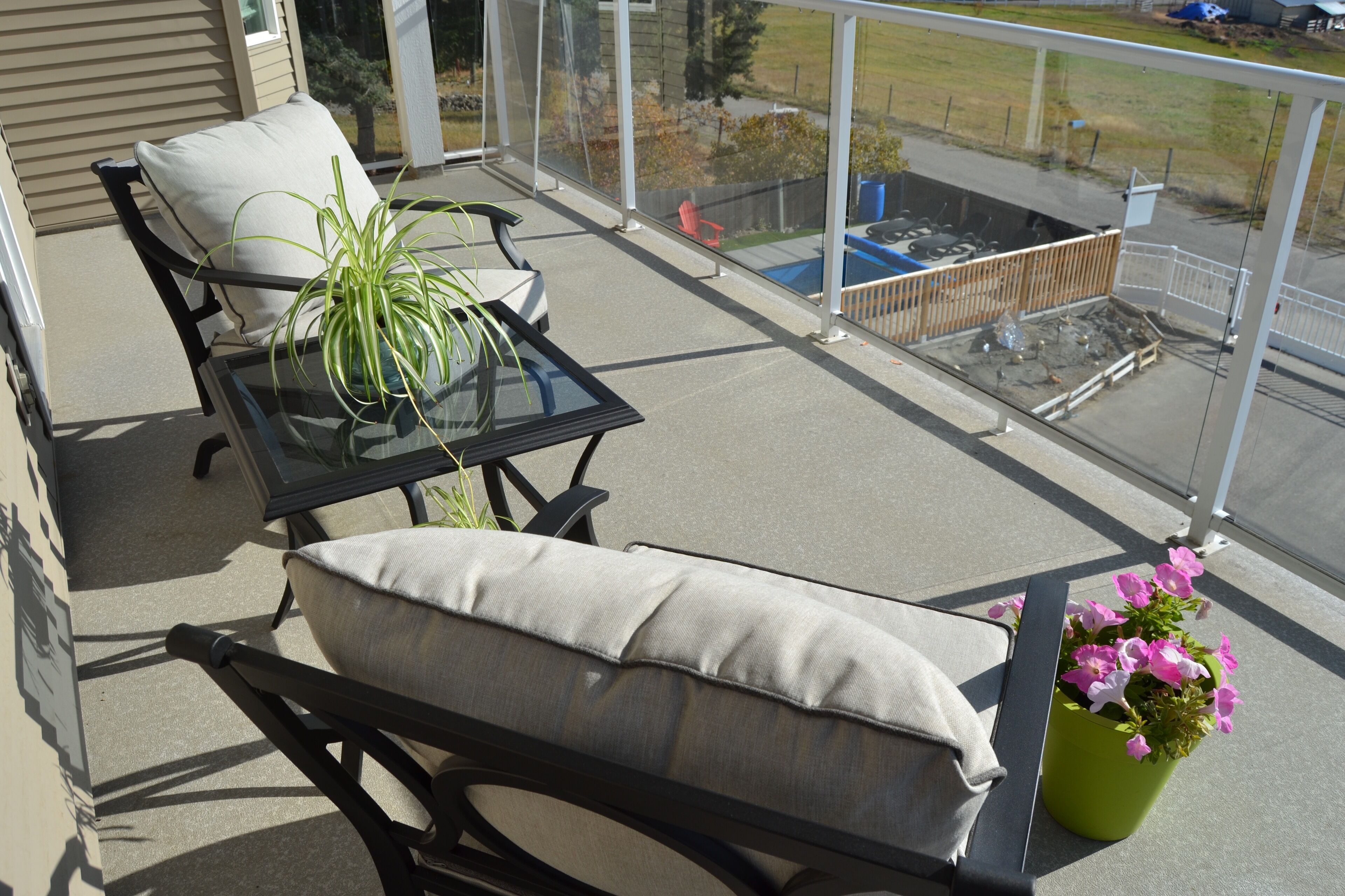 A balcony with a glass table, two chairs, a potted plant, and a flower pot.