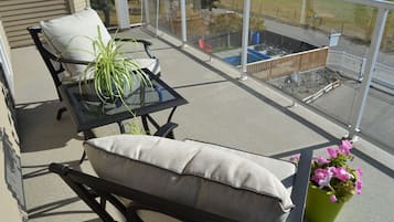 A balcony with a glass table, two chairs, a potted plant, and a flower pot.