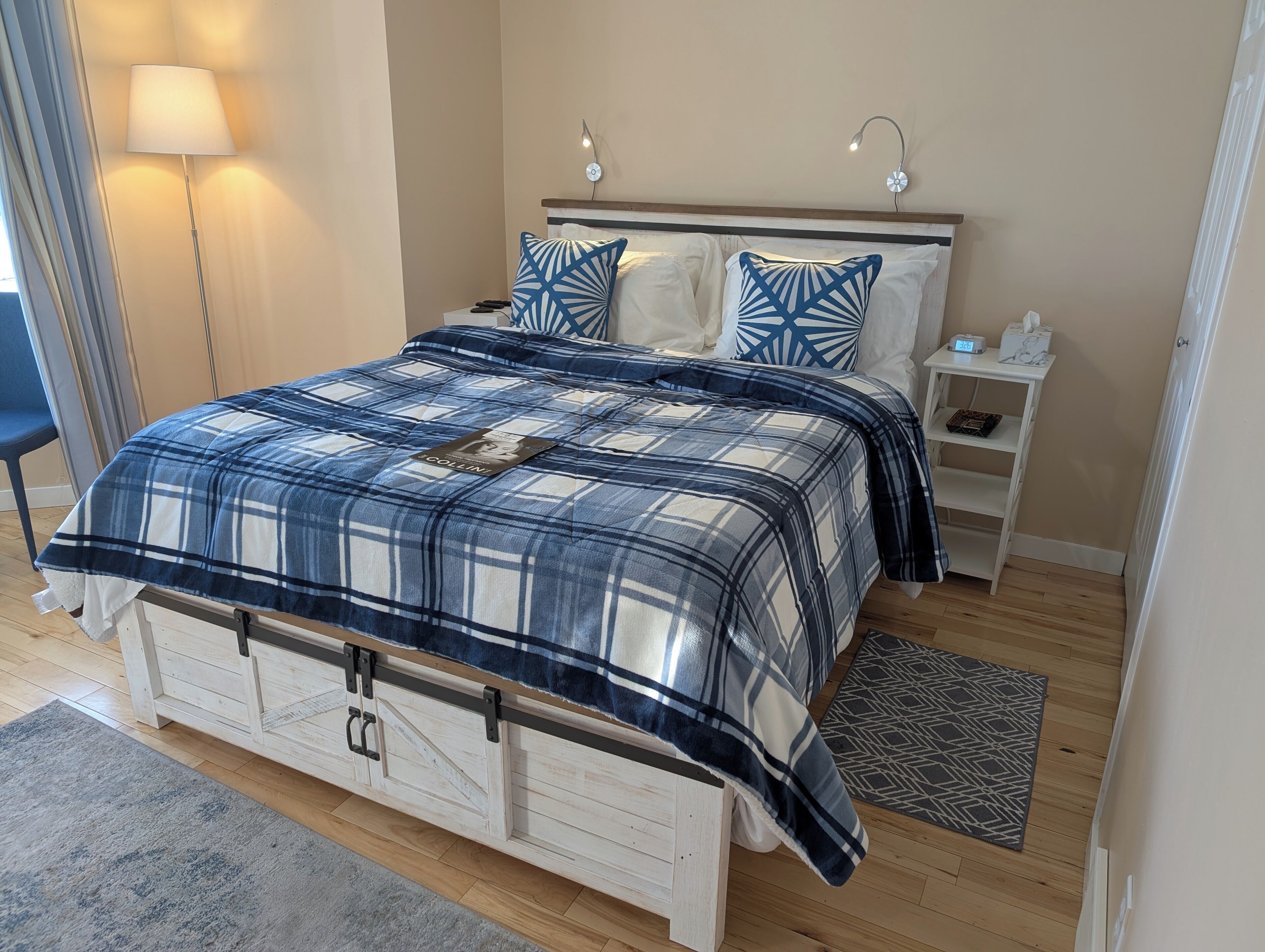 A bedroom with a plaid bedspread, two pillows, a bedside table, and a nightstand.