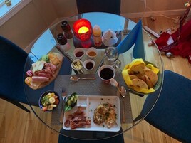 Una mesa de vidrio con una preparación para el desayuno, que incluye diversos alimentos, bebidas y condimentos.