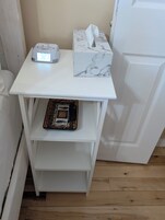 A small white bedside table with a digital clock, a tissue box, and a decorative tray.