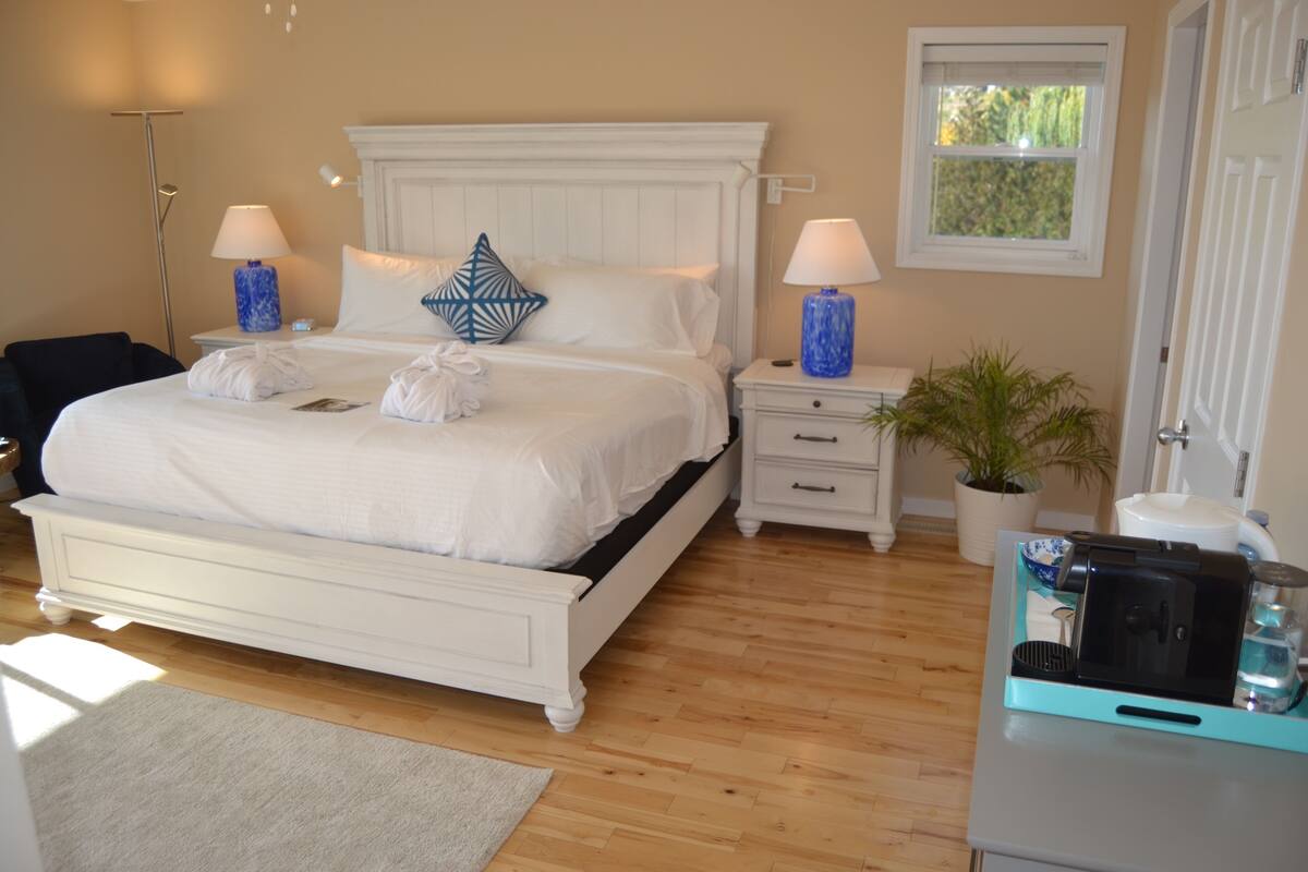 A neatly arranged bedroom with a large bed, bedside lamps, a potted plant, and a coffee maker on a table.