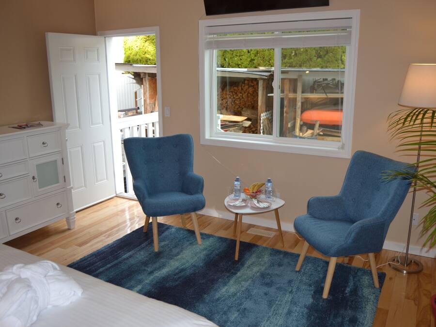 Hotelkamer met een bed, twee blauwe fauteuils, een tafeltje met waterflessen en fruit, een potplant en een raam met uitzicht op het landschap.