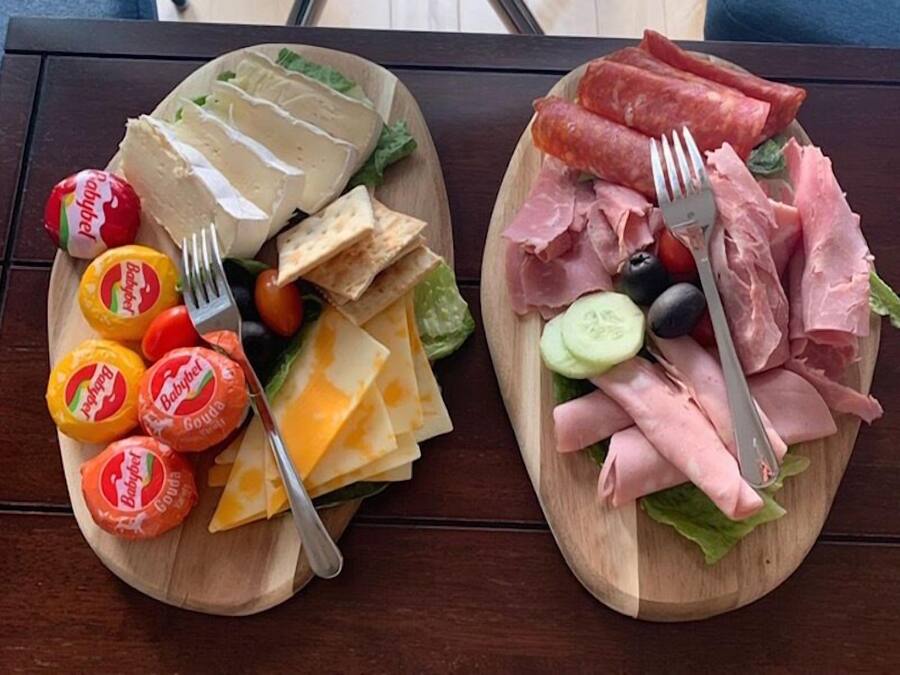 Kaksi puista tarjoilulautaa, joilla on erilaisia juustoja, leikkeleitä ja vihanneksia.