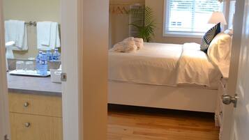 A bedroom with a bed, a window, a plant, and a bathroom with a sink and mirror.