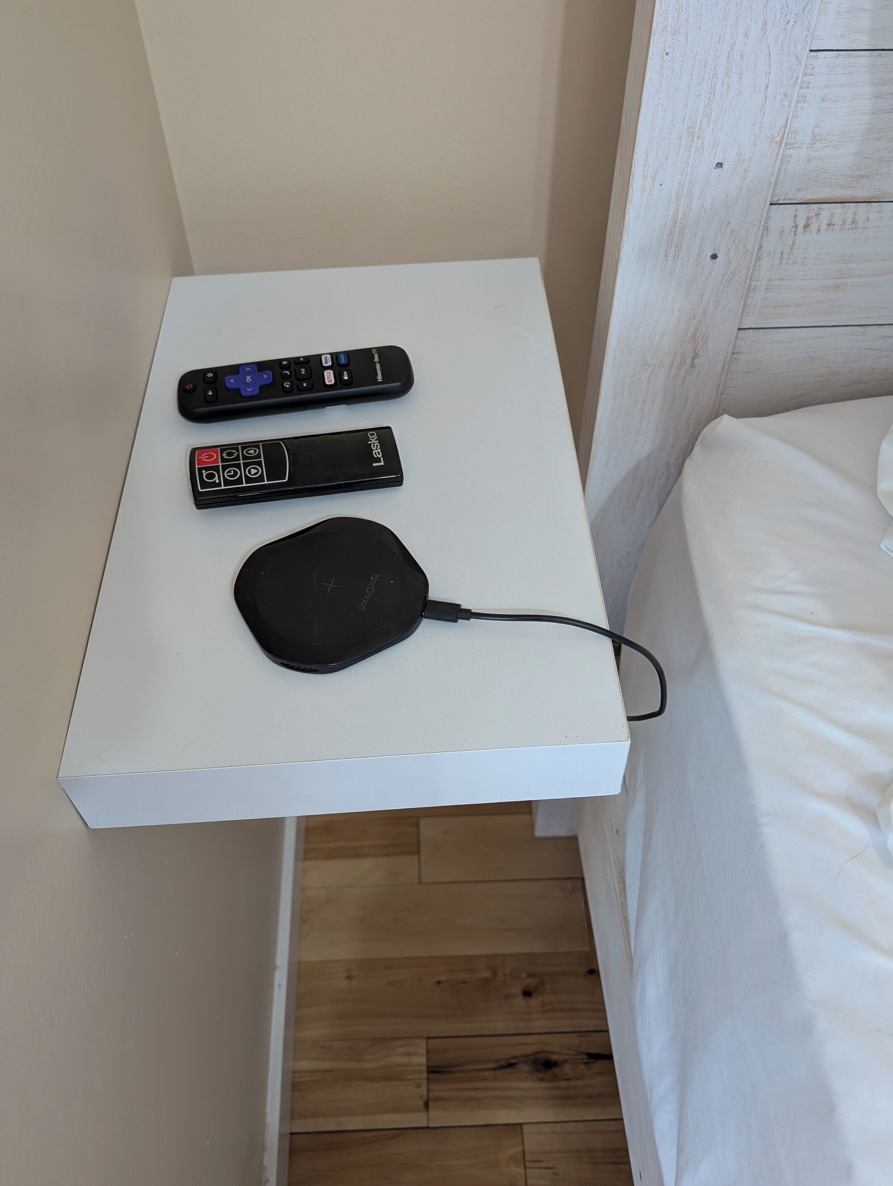 A small white table with two remote controls and a black charging device.
