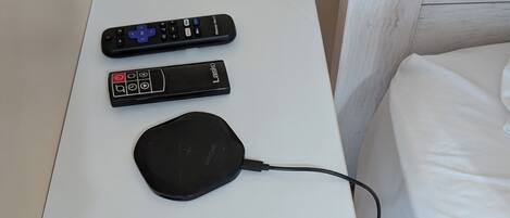 A small white table with two remote controls and a black charging device.