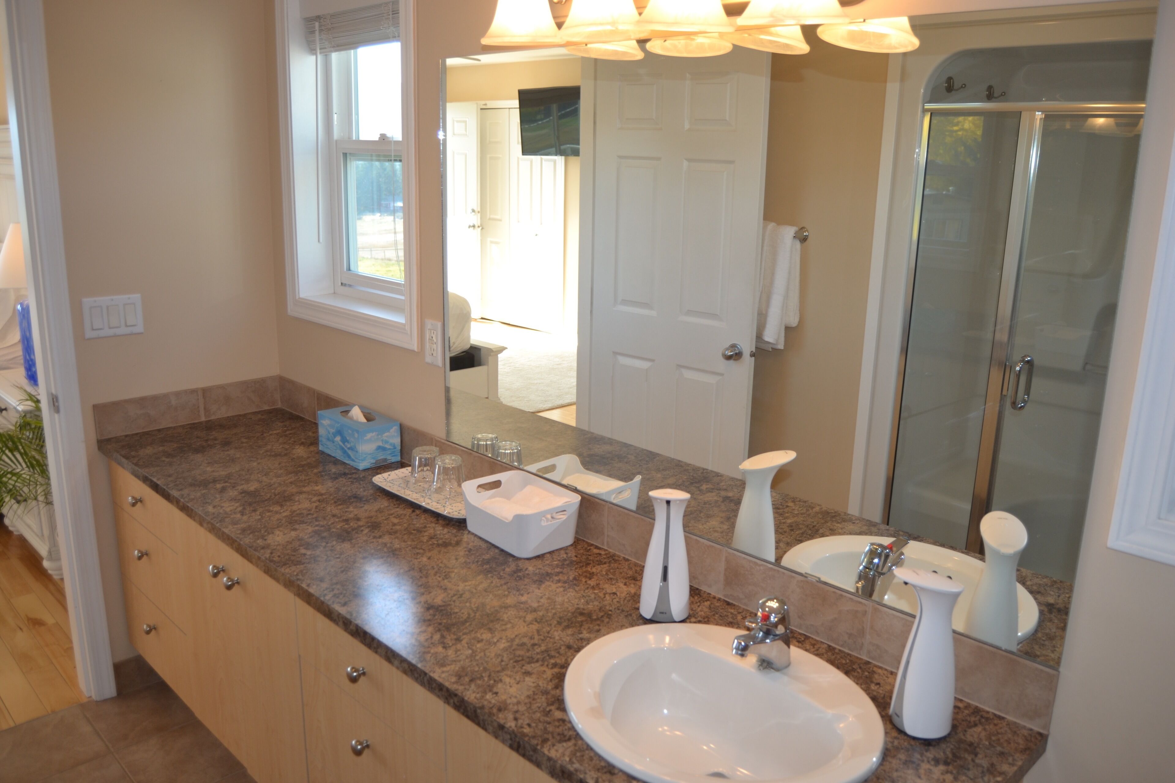 A bathroom with a granite countertop, a white sink, a mirror, and a glass shower enclosure.