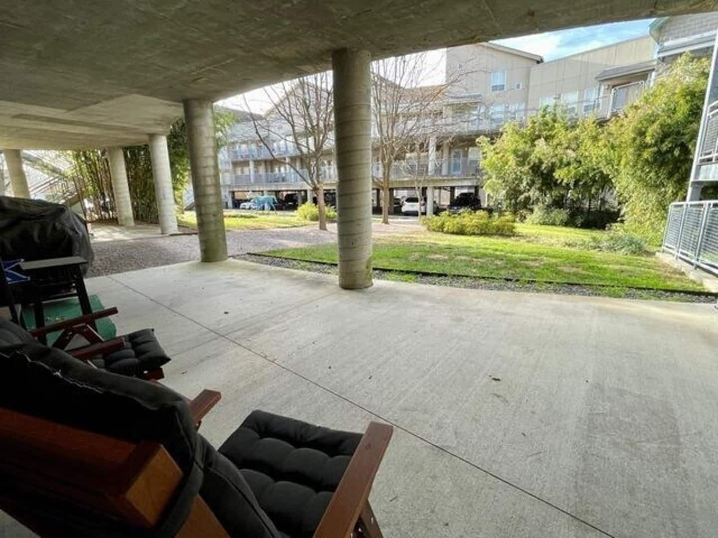 Un espacio al aire libre techado con pilares de concreto, una silla negra acolchada y una parrilla.